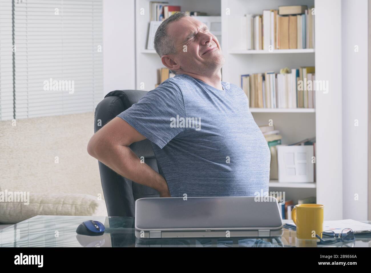 Man in home office suffering from low back pain sitting at a desk with