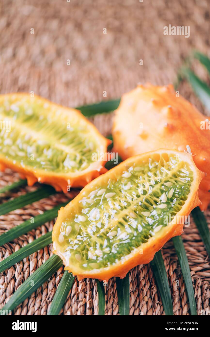 Kiwano or african horned melon with palm leaves on rattan background. Cutted hedged gourd