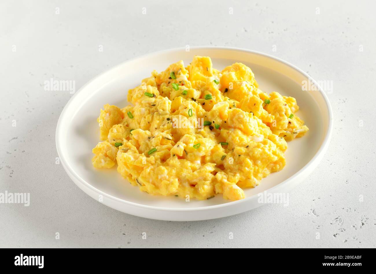Scrambled eggs on plate over white stone background, close up view Stock Photo