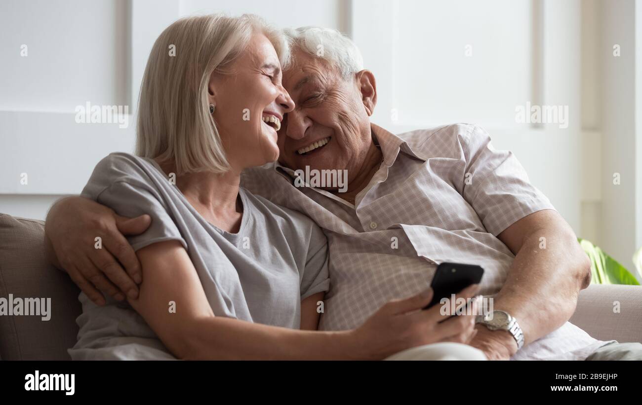 Happy older wife and husband cuddling, using phone together Stock Photo