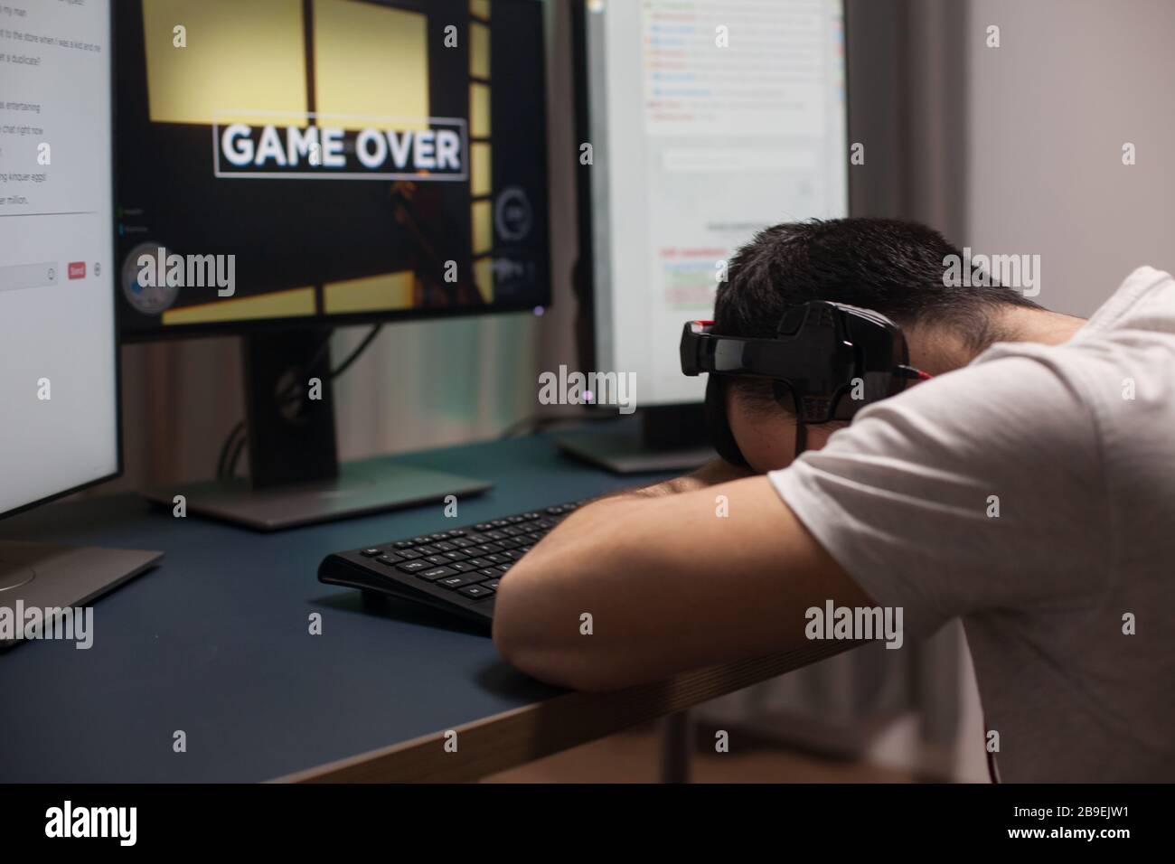 Man keeping his head on the office after losing at shooter games on the stream. Game over for professional gamer. Stock Photo