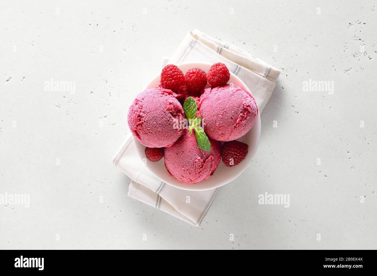 Raspberry ice cream scoop with fresh raspberries in bowl over white stone background with free text space. Top view, flat lay Stock Photo