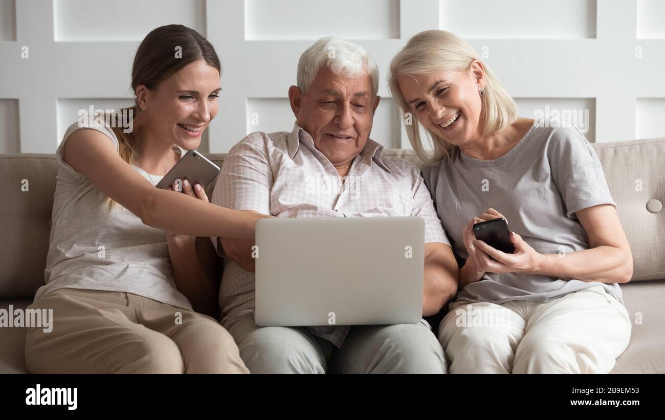 Happy older parents with adult daughter using electronic devices Stock