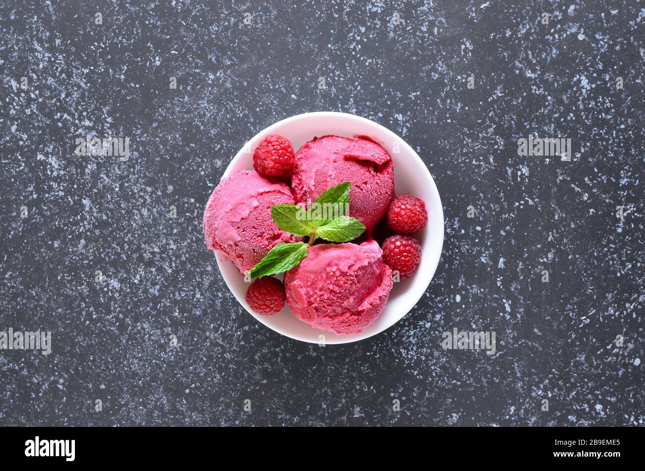 Raspberry ice cream scoop with fresh raspberries in bowl on stone background with copy space. Cold summer dessert. Top view, flat lay Stock Photo