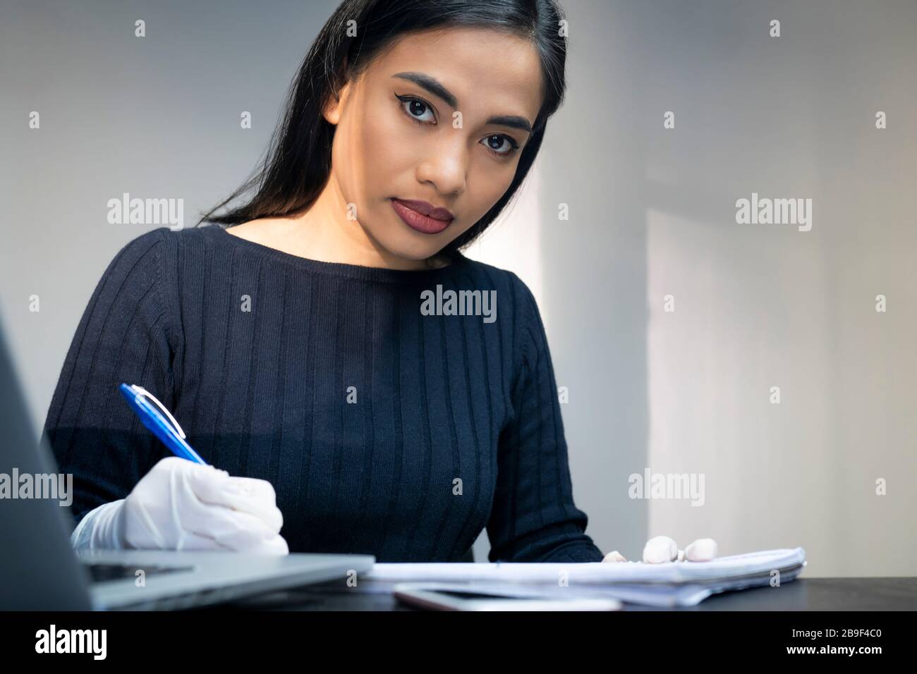 Coronavirus outbreak. Beautiful asian woman working at home during the lockdown. Wearing disposable medical gloves. Stock Photo