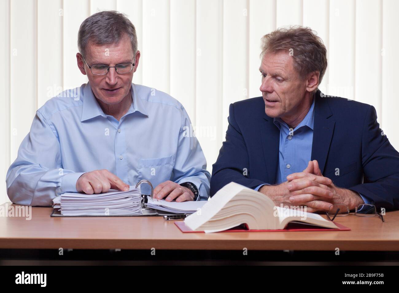 Two mature businessmen or partners discussing a projekt sitting at a desk with folder and book Stock Photo