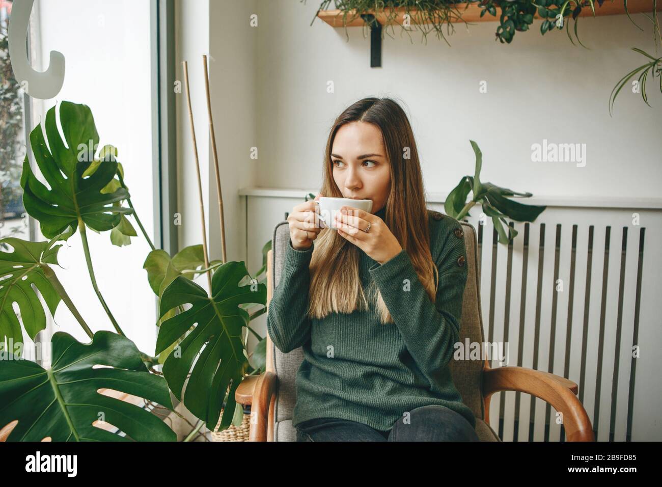 A girl sits in a cafe and drinks a hot drink. She is waiting for someone and she has a meeting or enjoys her morning drink. Stock Photo