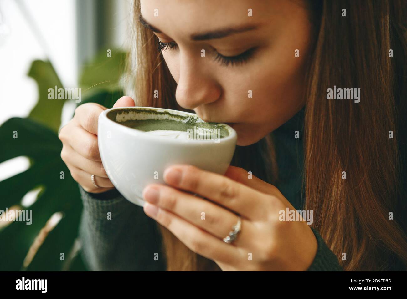 Close-up face or portrait of a girl who drinks healthy and delicious green matcha latte tea Stock Photo