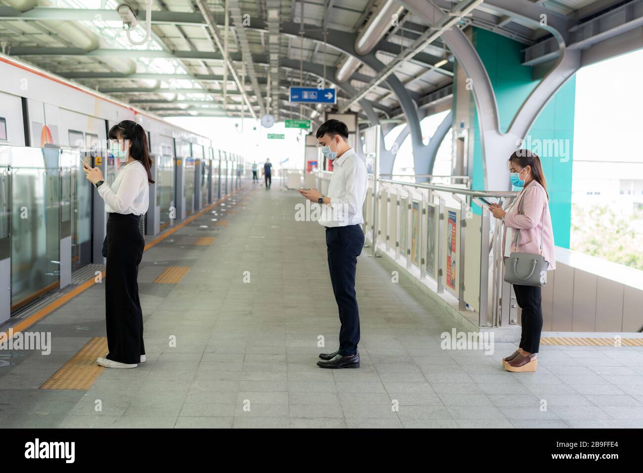Three Asian people wearing mask standing distance of 1 meter from other people keep distance protect from COVID-19 viruses and people social distancin Stock Photo
