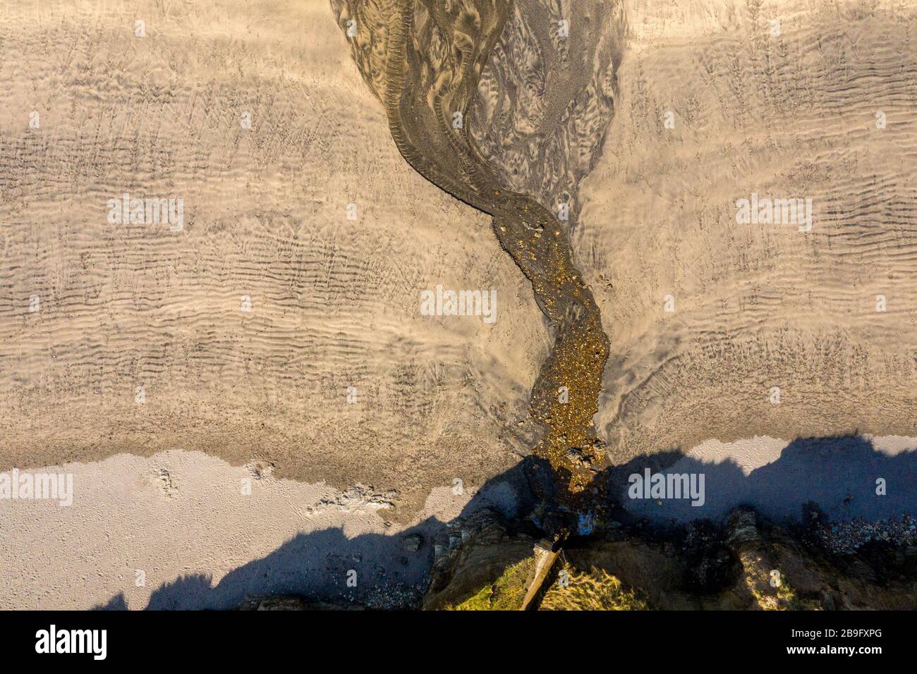 Aerial image of water outlet of cliffs and stream over golden sand Stock Photo