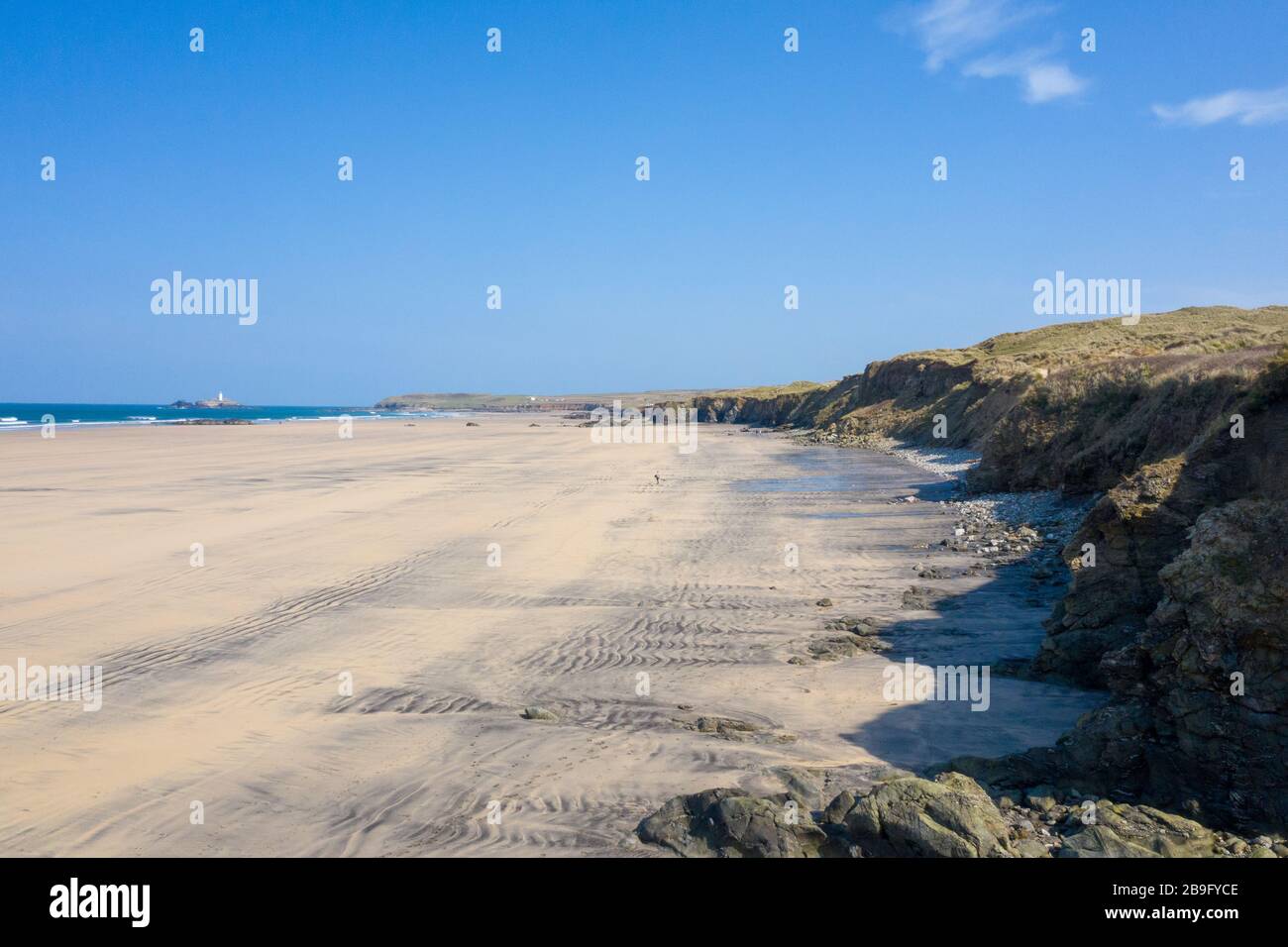 aerial photo of an empty Gwithian beach with waves breaking and godrevy lighthouse in the background and sand dunes on the right on a blue sky day Stock Photo