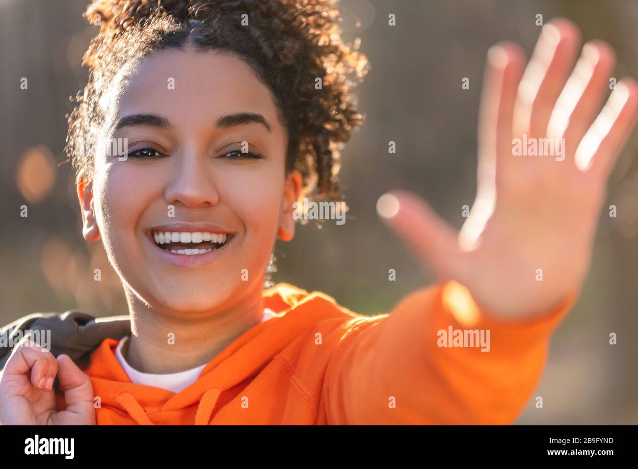 Outdoor portrait of beautiful happy mixed race African American girl teenager female young woman laughing, waving and smiling with perfect teeth in go Stock Photo