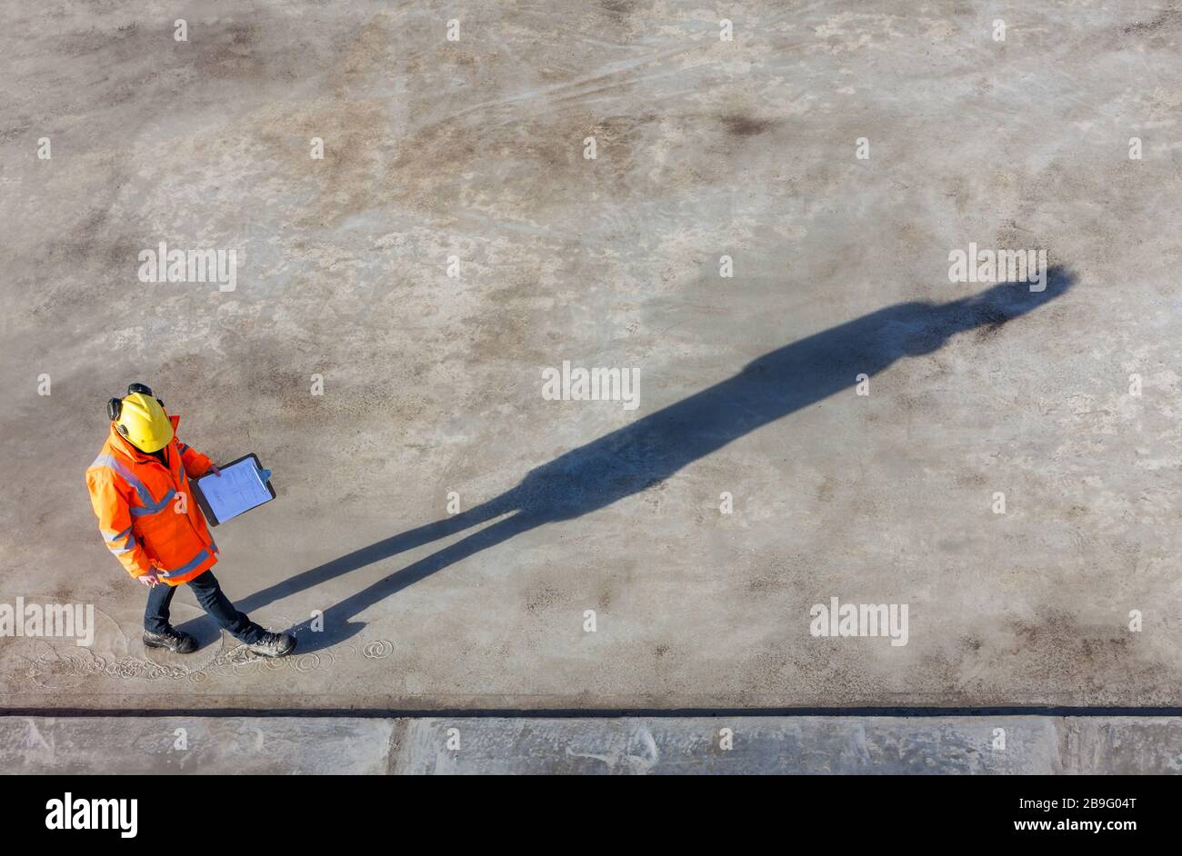 Overhead aerial view of anonymous construction worker or builder wearing a hi vis jacket, a hardhat and carrying a clipboard on a building site with t Stock Photo