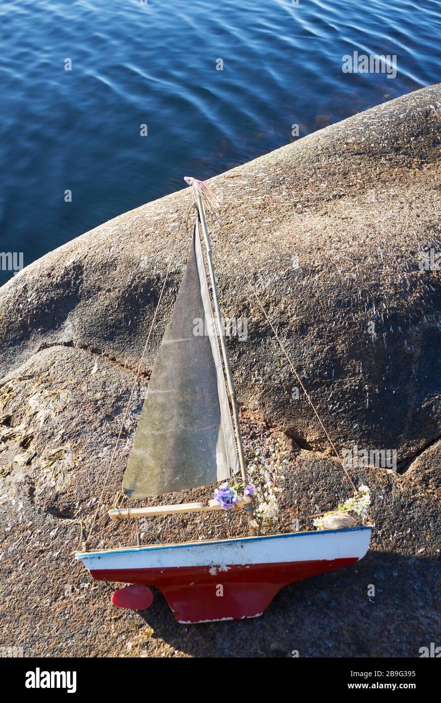 Toy sailboat with flowers on lakeside rock Stock Photo