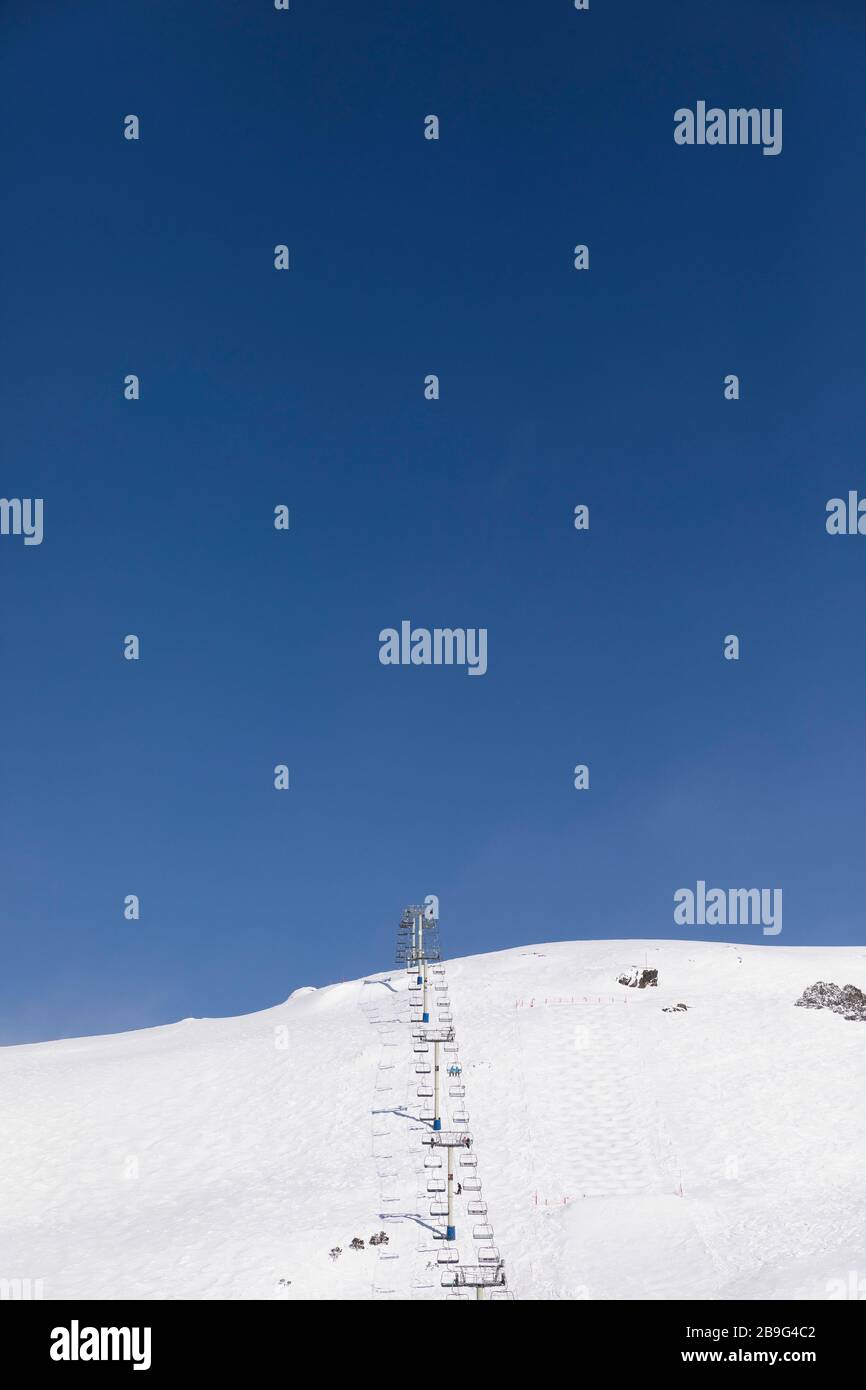 Ski lift on snowy mountain slope below sunny blue sky, Falls Creek, Victoria, Australia Stock Photo
