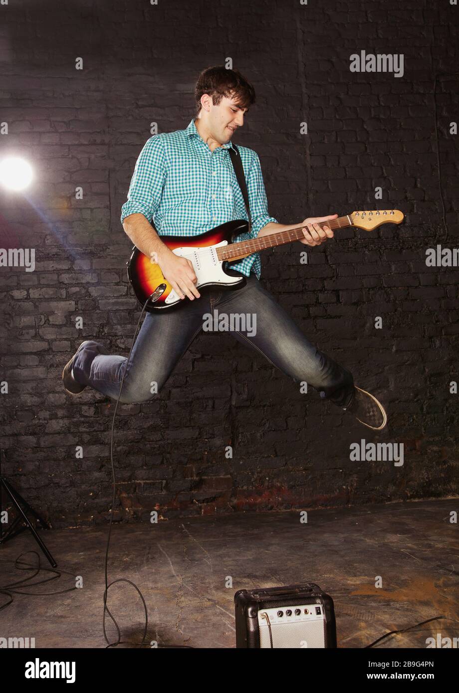 Teenage boy playing electric guitar and jumping above amplifier Stock