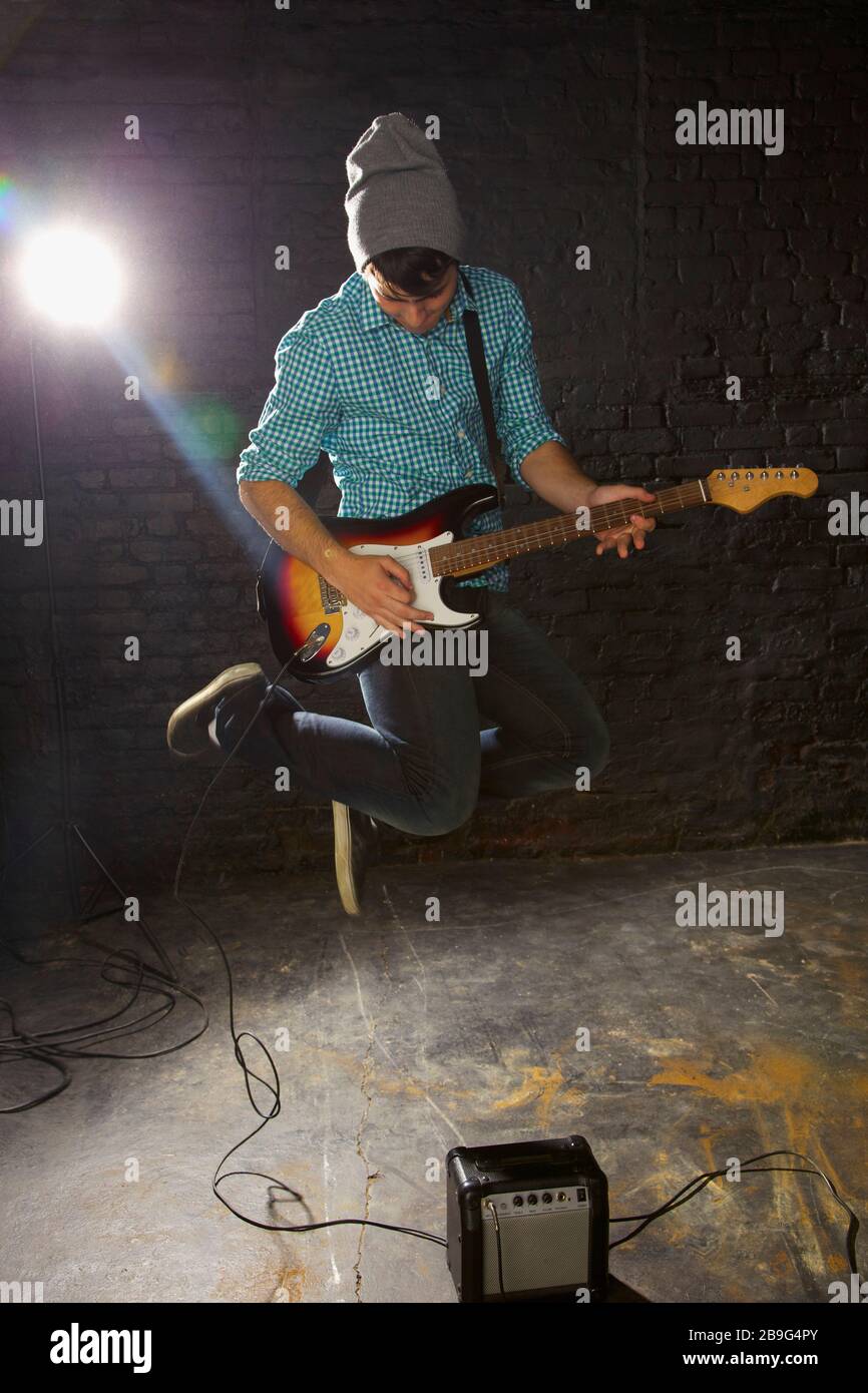 Teenage boy playing electric guitar, jumping above amplifier Stock