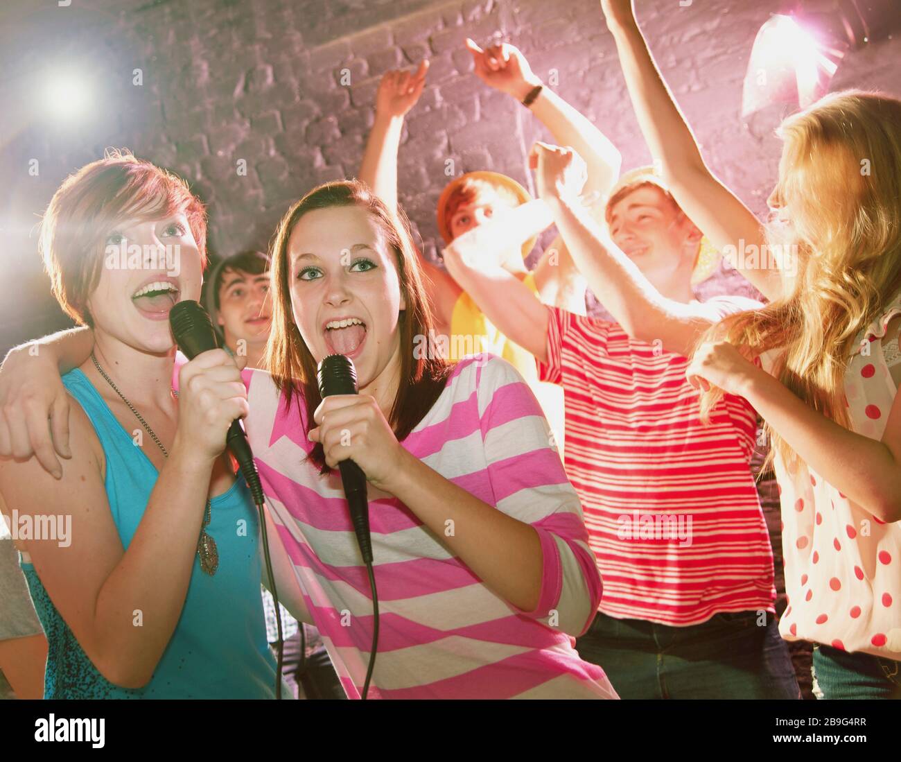 Happy teenage friends singing karaoke at party Stock Photo