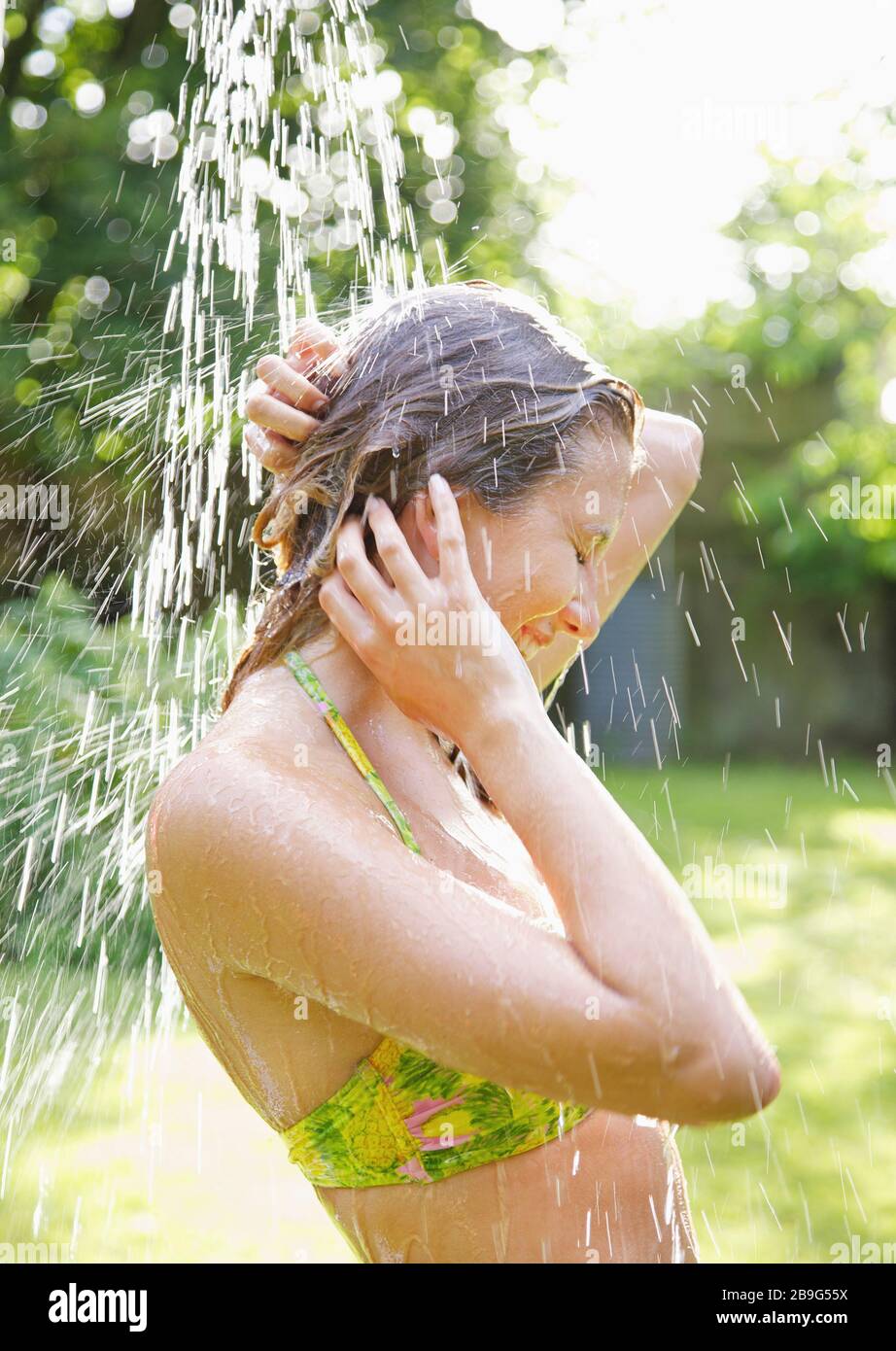 Young woman in bikini top standing under outdoor shower on summer patio Stock Photo