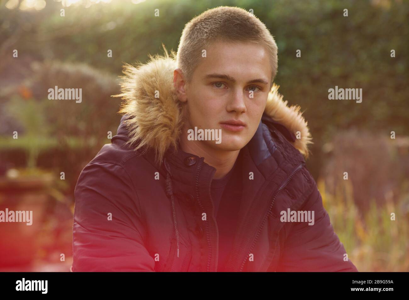 Portrait confident teenage boy in jacket with fur hood in park Stock Photo