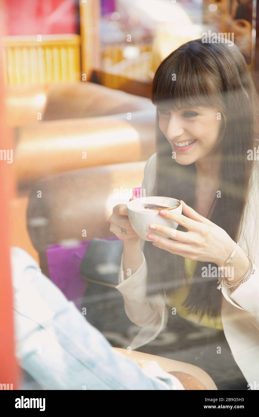 Happy young woman enjoying cappuccino in cafe window Stock Photo