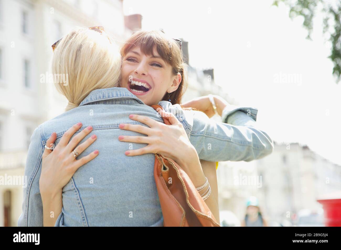 Happy young women friends hugging on sunny urban sidewalk Stock Photo