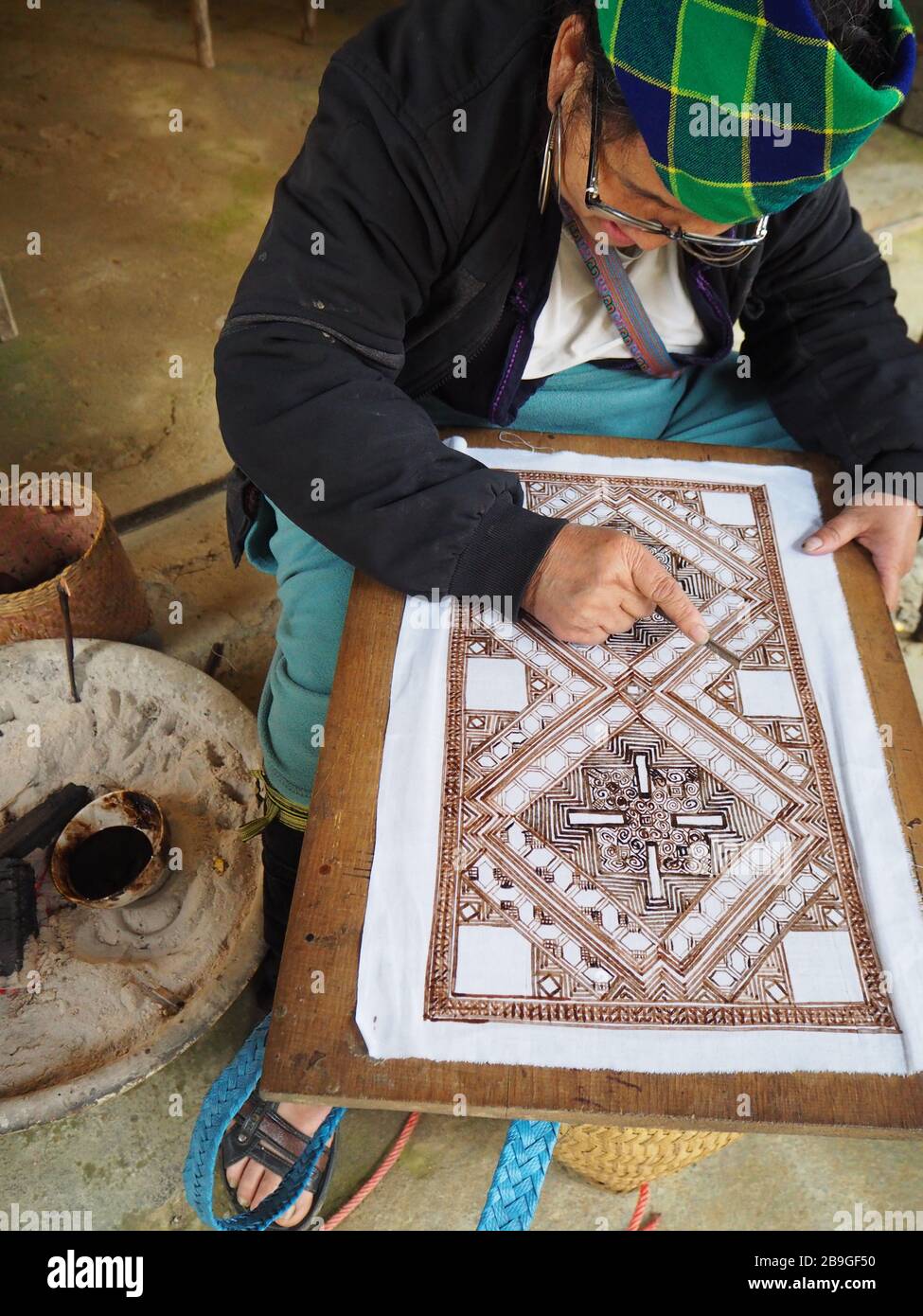 A Hmong woman using traditional patterns to paint on fabric in Sapa, Vietnam which she will then make into bags and other handicrafts Stock Photo