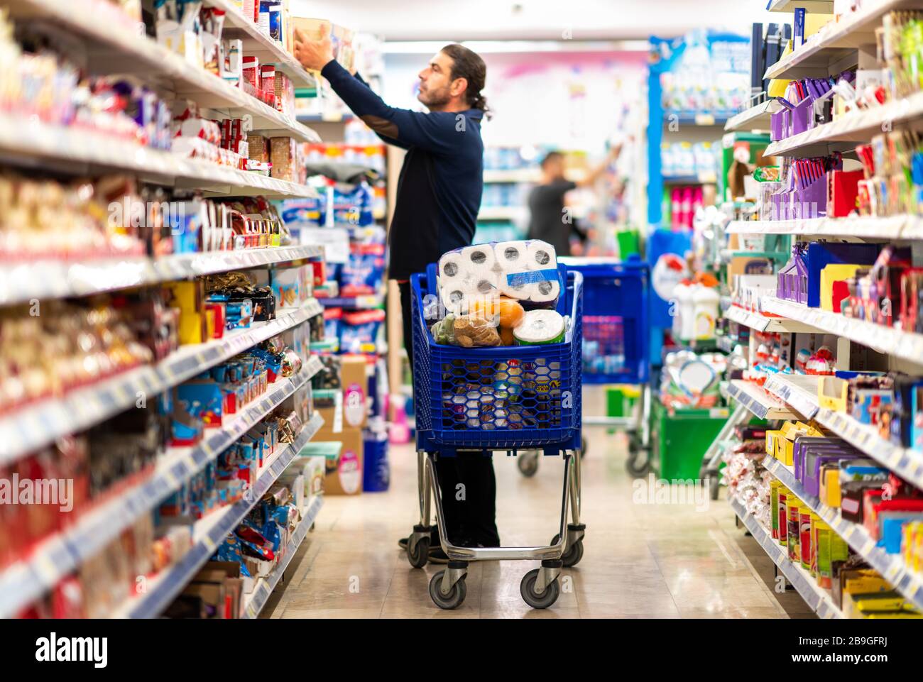 Full shopping cart, customer is stocking vital needs because of global chaos. Shopping with blur supermarket store products, interior background Stock Photo