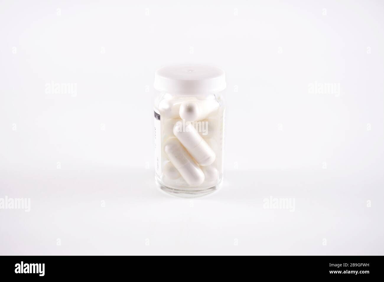 Glass pill bottle full of white capsules (frog eye view on white background) Stock Photo