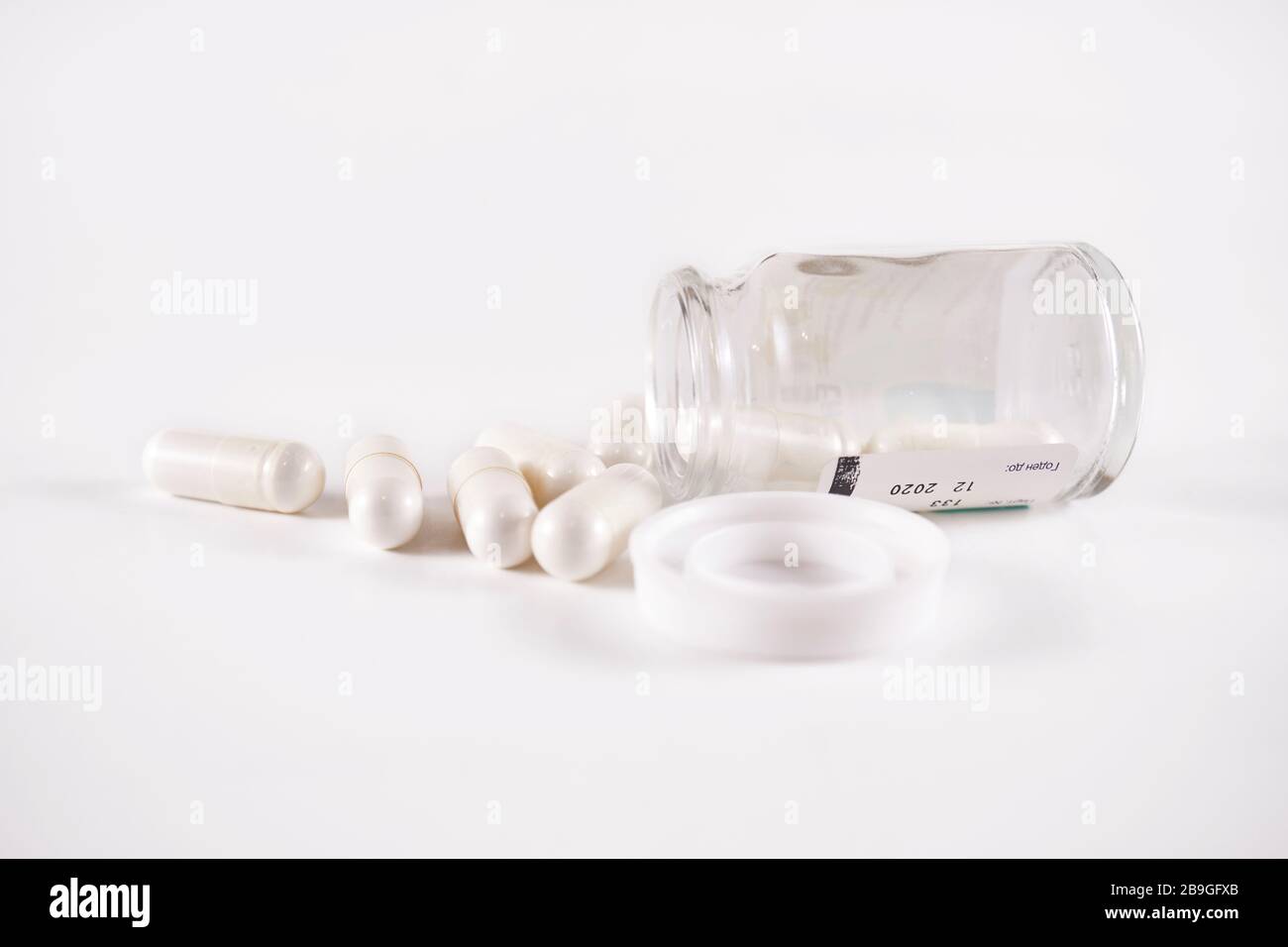 White capsules spilling out of fallen glass bottle (frog eye view on white background) Stock Photo