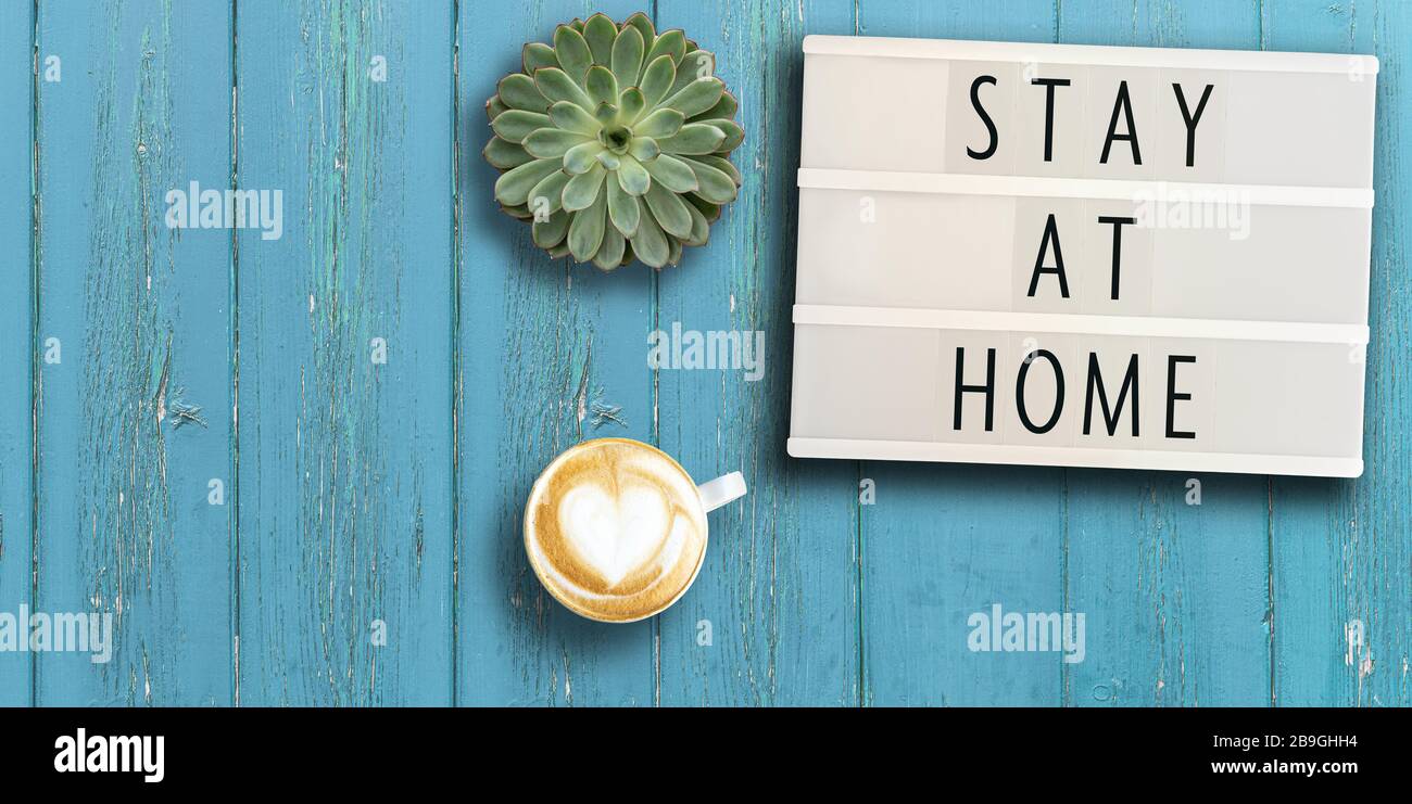 lightbox with appeal text STAY AT HOME on rustic wooden table with potted plant and coffee, social distancing concept during coronavirus pandemic Stock Photo