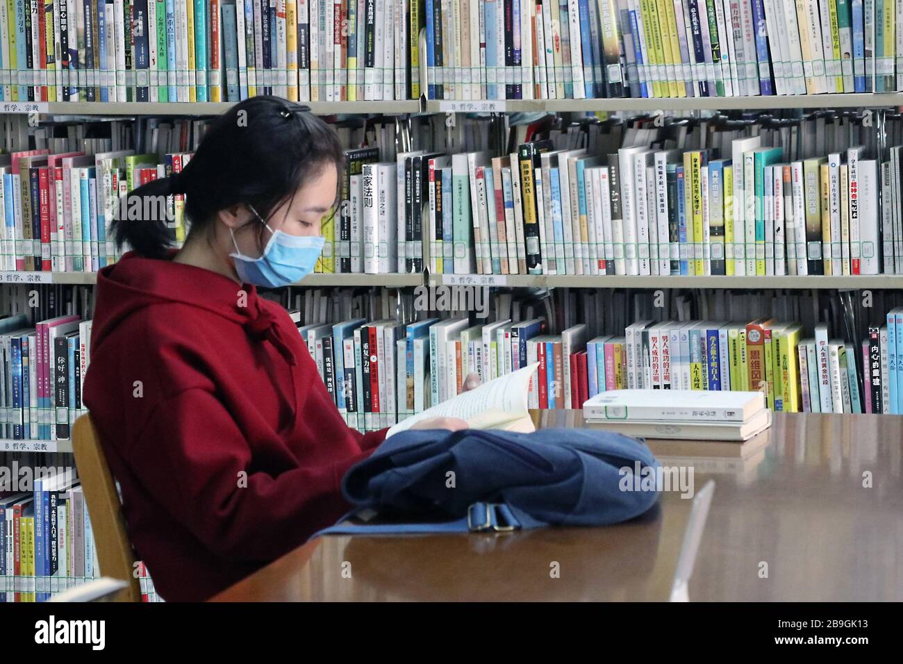 Hefei, China's Anhui Province. 24th Mar, 2020. A reader reads a book at Anhui Provincial Library in Hefei, east China's Anhui Province, March 24, 2020. The library reopened on Tuesday under strict measures taken to fight against the COVID-19. It is allowed to receive no more than 1,200 readers per day and 220 people in real time. Readers are required to wear face masks, display their identity card or reader card, take temperature checking and verify their health QR code before entering the library. Credit: Han Xiaoyu/Xinhua/Alamy Live News Stock Photo