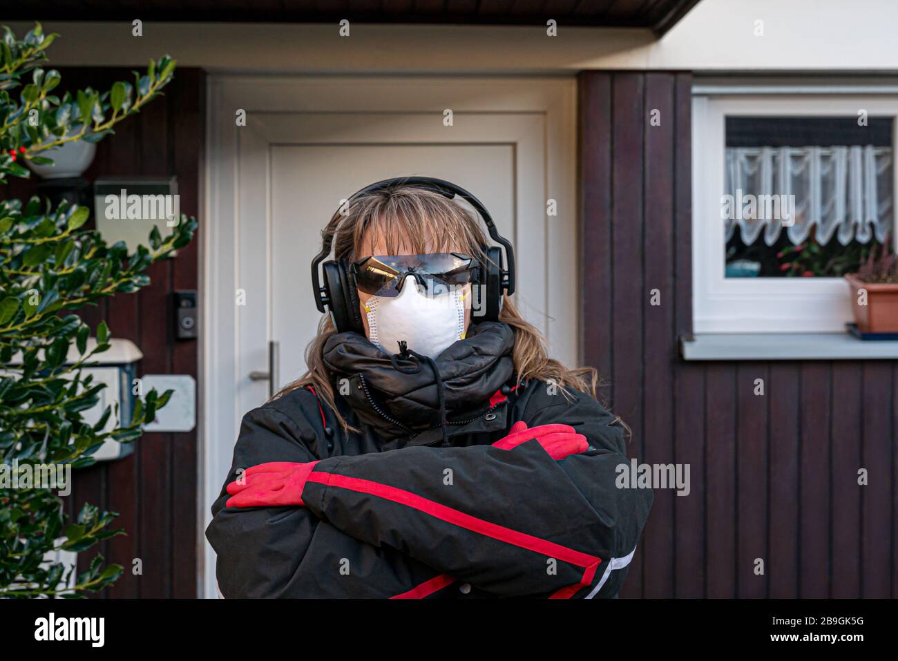 A woman walks out the door. She protects against the Corona Virus. Panicked citizen. She wears headphones, glasses, a protective mask, rubber gloves, Stock Photo