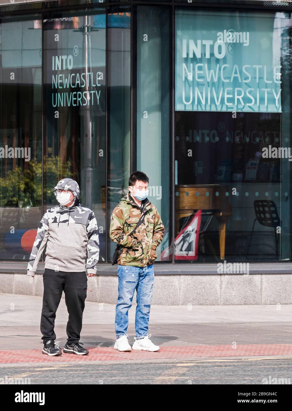 Newcastle upon Tyne, UK, 22nd March 2020. Two asian males wait to cross a road wearing protective masks during the covid-19 pandenic. Joseph Gaul/Alamy News Stock Photo