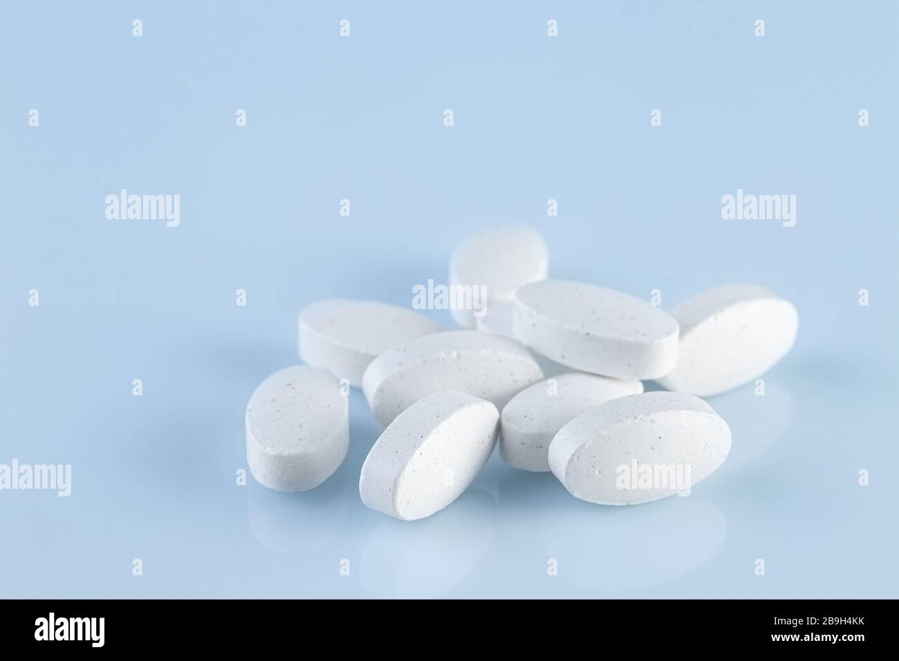 Heap of white medical pills on a light blue background. Pharmaceutical medicament, cure for health. Medicine concept. Stock Photo