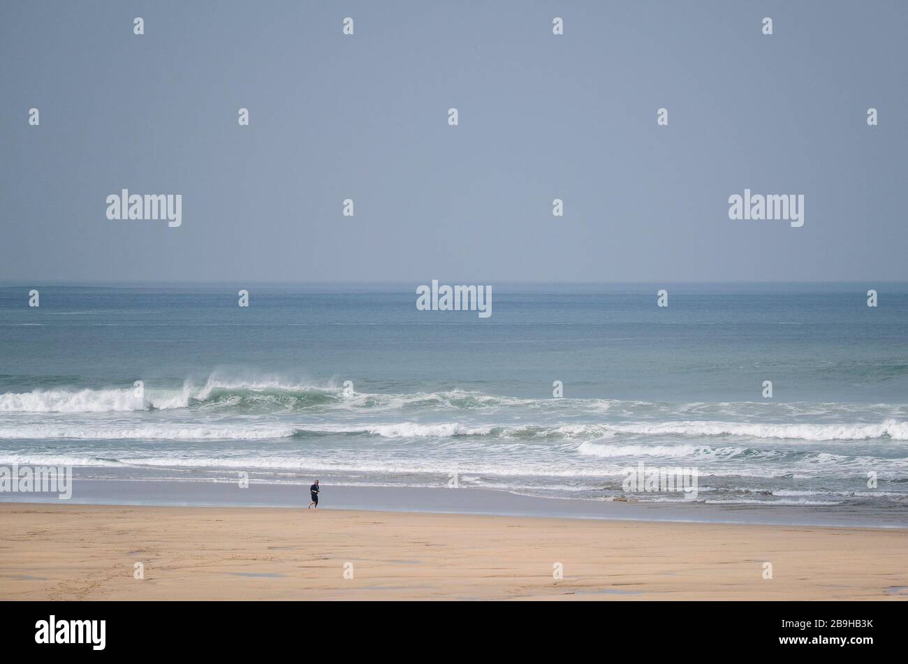 Newquay, Cornwall, UK. 24th March, 2020.  A local resident taking the Government advice and ensuring he is self-isolating as he runs along the shoreline on a completely empty Fistral Beach in Newquay in Cornwall.   Gordon Scammell/Alamy Live News. Stock Photo