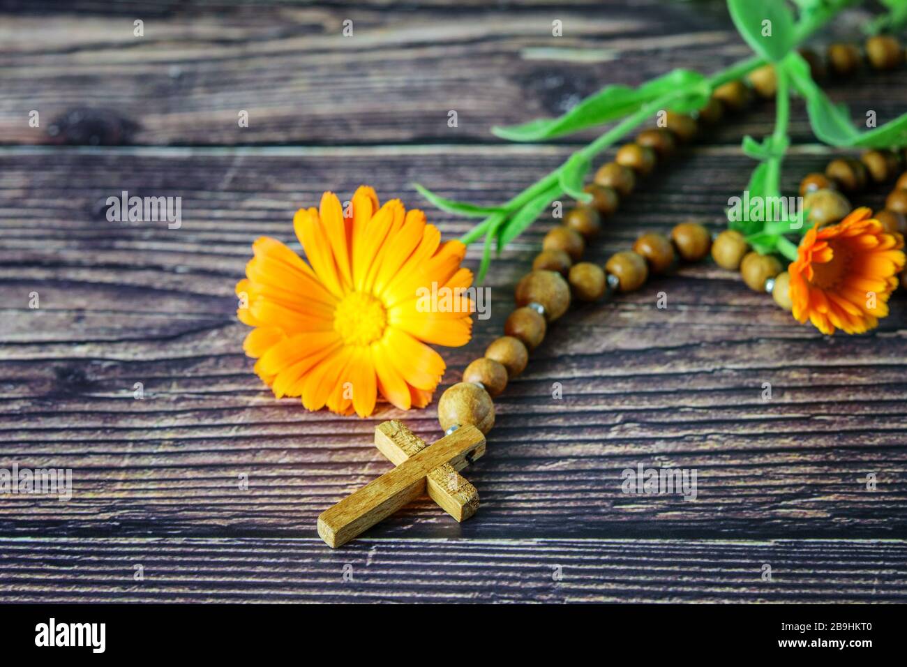 Wooden christian cross with chaplet and a flower on the wood background closeup. Christian religion concept, easter. Stock Photo