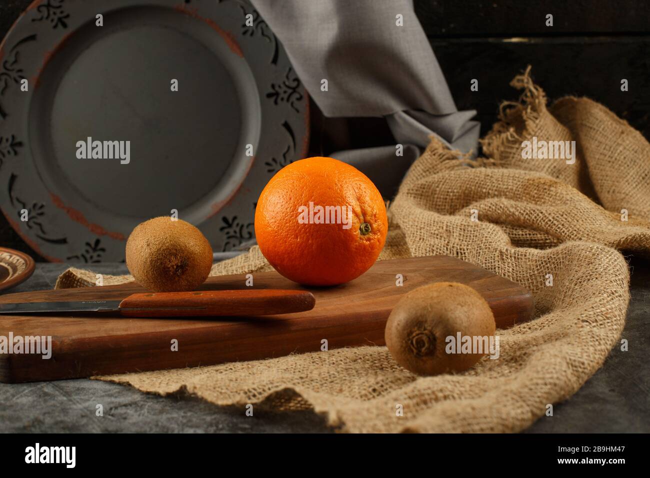 Orange and kiwies on a wooden board with a knife around. Stock Photo