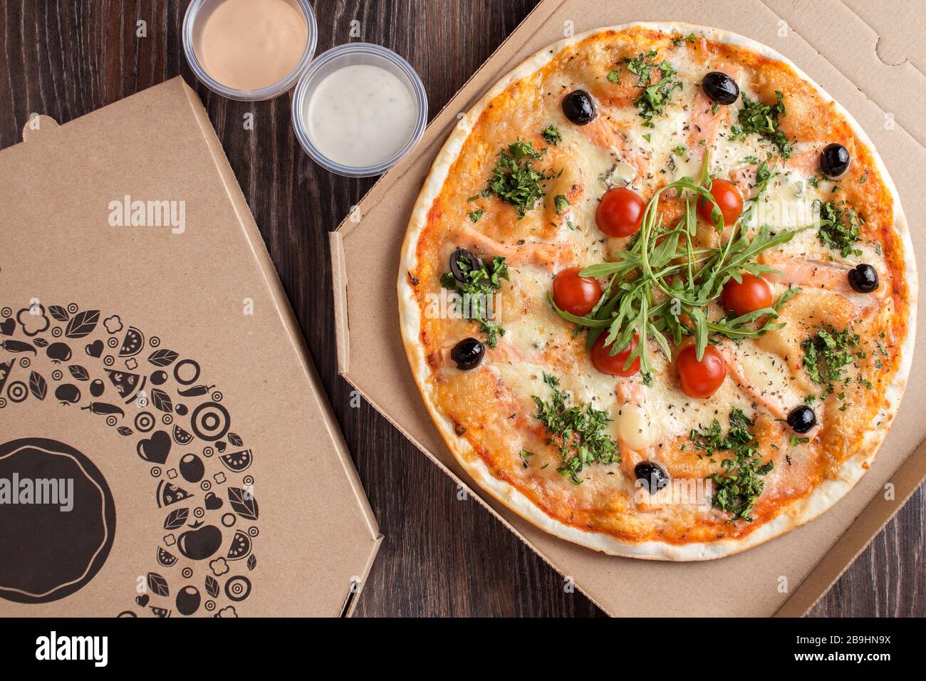 Thin crust pizza with seafood salmon and arugula in cardboard delivery