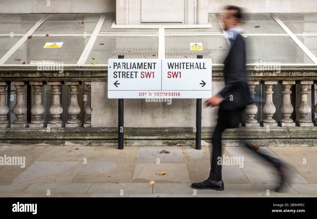 London civil servant. A suited office worker passing a street sign for Parliament Street and Whitehall in the civil service district of Westminster. Stock Photo