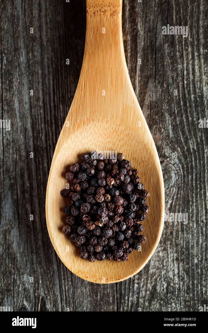 Black pepper spice peppercorn on wooden spoon and dark rustic