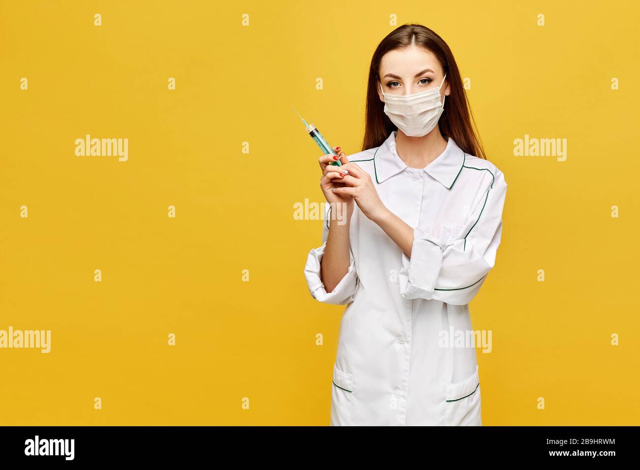 Young woman in medical clothes and protective mask posing with a ...