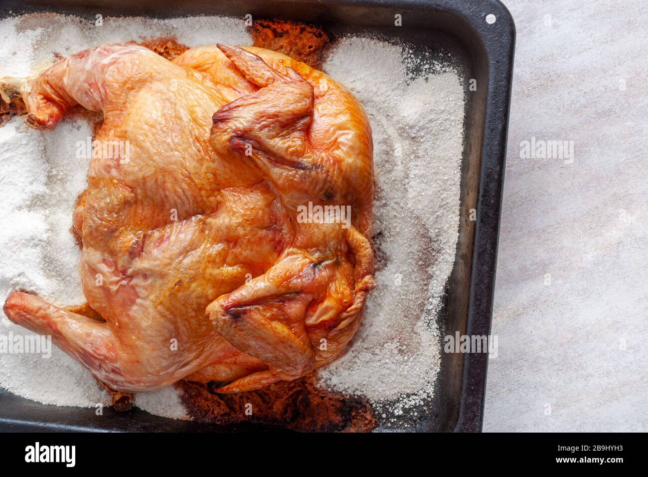 Chicken baked in the oven on a thick layer of salt on a metal tray. The view from the top. Stock Photo