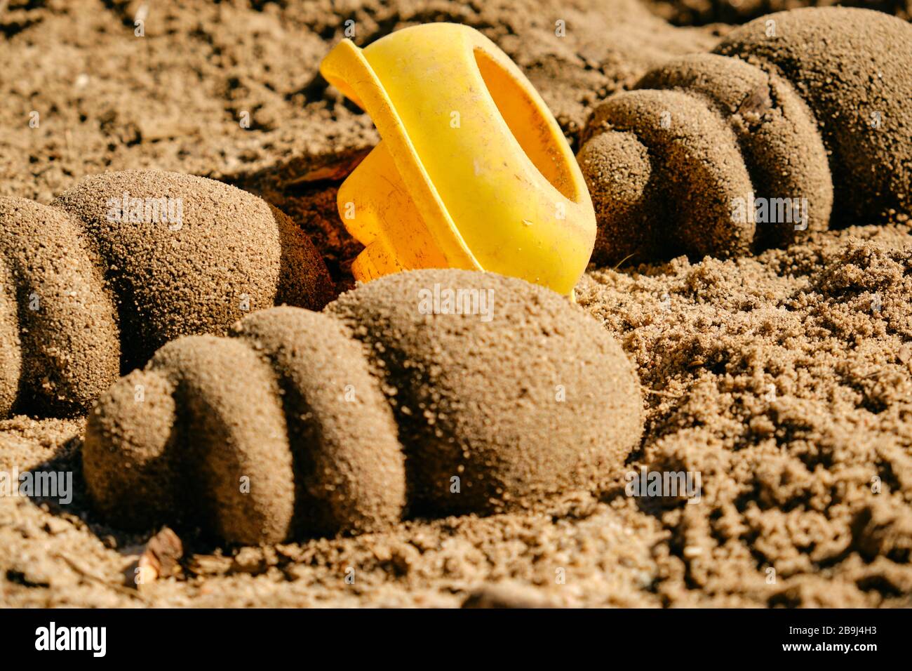 Used yellow toy boat lying upside down between sand shells on the sandy ground in the sun. Seen in Germany in March. Stock Photo