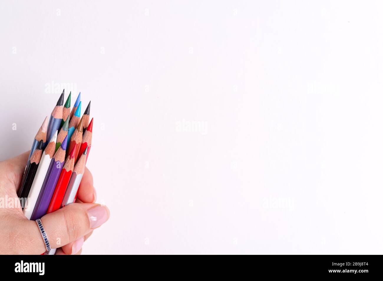 Woman's hand is holding bunch of multicolored sharp pencils for art creativity on a white background with copy space. Top view. Stock Photo