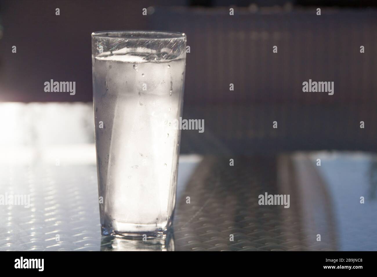 Tall Icy Cold Glass of Water with Water Drops Reflecting on Glass Table