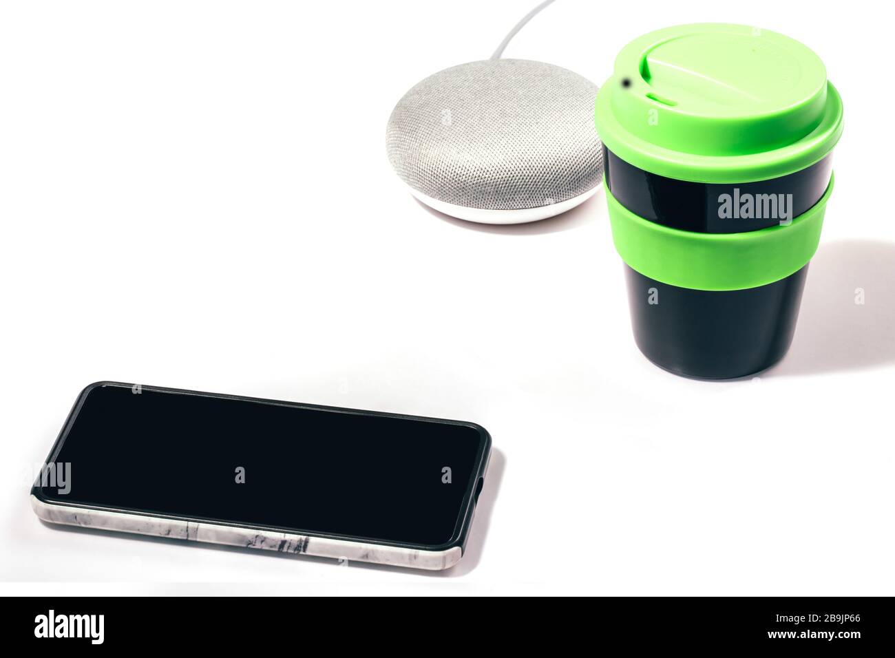 Digital Assistant concept. Smart speaker with smartphone and reusable coffee cup with green lid on white background. Stock Photo