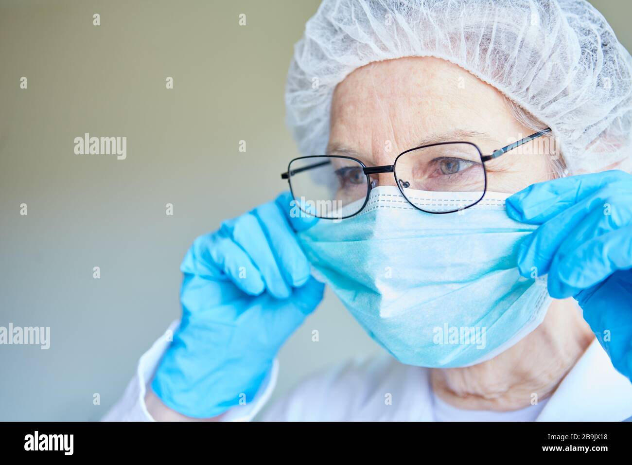 Old doctor in protective clothing puts on mouth protection in the intensive care unit of a clinic Stock Photo