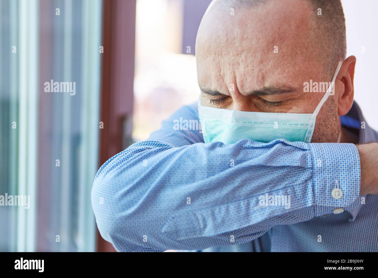 Mann mit Covid-19 beim Husten in Armbeuge während Coronavirus Epidemie Stock Photo