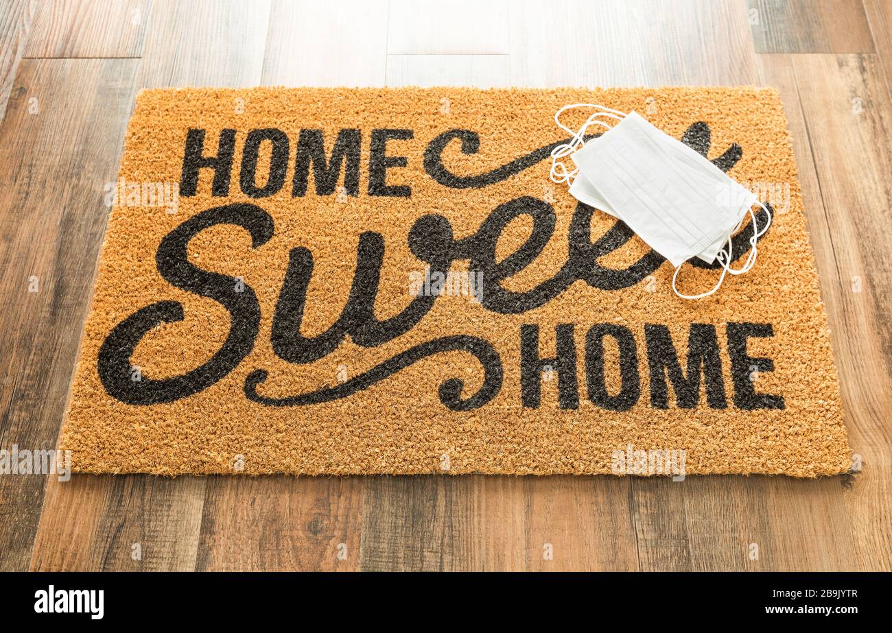 Several Medical Face Mask Rests on Home Sweet Home Welcome Mat Amidst The Coronavirus Pandemic. Stock Photo